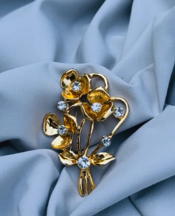 Gold-tone flower brooch with crystal accents on blue fabric