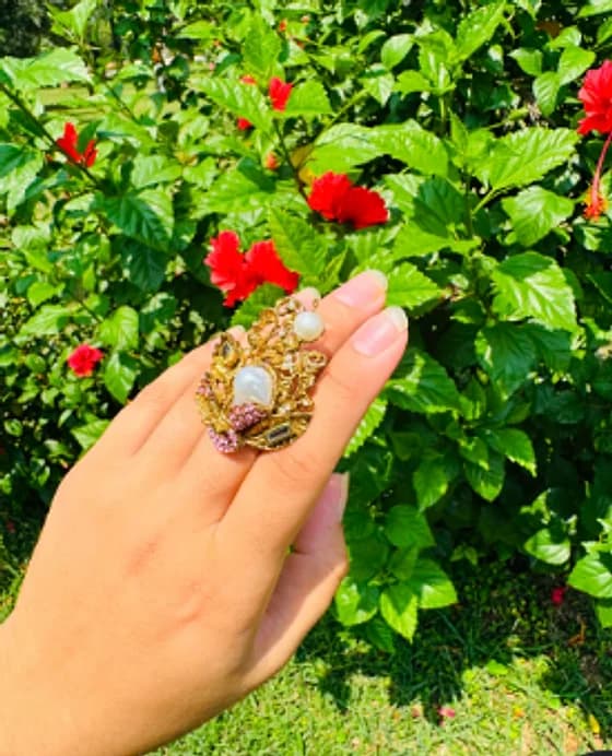Hand wearing a gold-tone statement ring with a pearl-look centre